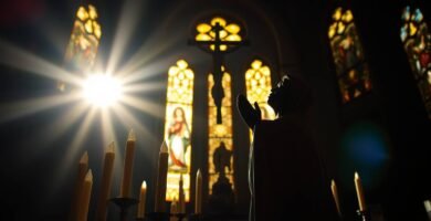 Bild des Inneren einer Kirche im Morgengrauen mit einem Priester, der mit seinen Händen zum Himmel betet, und einem intensiven Lichtstrahl, der durch eines der Fenster einfällt